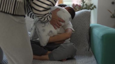 Anne yeni doğmuş bebeği kanepede küçük kardeşe veriyor, aile bağı, hassas an, yuva kurma, kardeş sevgisi, sevgi dolu jest, rahat oturma odası, aile bakımı, yeni ekleme