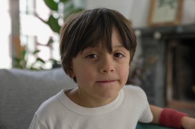 Siyah saçlı, beyaz gömlekli, yakın plan, kapalı mekan, tarafsız yüz ifadesi, yumuşak ışıklandırma, gündelik ortam, arka plan bulanık, doğal ve samimi an, nazik ve sakin ruh hali