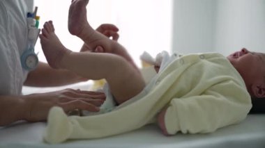 Yeni doğmuş bir bebek hemşireden bez değiştiriyor. Yeni doğan bakımının rutin ama önemli bir parçası. Bebek bakımında gereken hassasiyeti ve dikkatli davranışı vurguluyor.