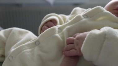 Yeni doğmuş bebek yumuşak bir kıyafetle dinlenirken parmağına tutunuyor. Yakın plan, küçük, narin eli ve hassas anı yakalar. Yetiştirici bir ortamda doğan bir bebeğin hassasiyetini ve masumiyetini vurgular.