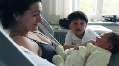 Anne ve büyük kardeş hastane yatağında yeni doğan bebeğe hayran. Sevecen bir etkileşim ailenin neşesini ve kardeşler arasındaki yakın bağı vurgular. Yürek ısıtan bir sevgi ve bağ anını yakalar.