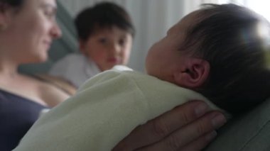 Anne ve büyük kardeş yeni doğan bebeğe bakıyor, aile içi sevgi ve hastane yatağında bir bağ yakalıyorlar. Anne, büyük çocuk ve yeni doğan arasındaki hassas etkileşim ve bağ