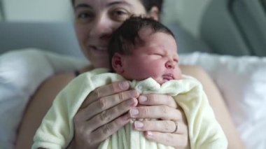 Anne yeni doğmuş bebeğini neşeyle hastanede tutuyor. Anneler gururla gülümserler ve bebek içerikli ifade anne sevgisinin ve bağlantının hassas bir anını yakalar. 