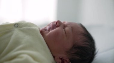 Yeni doğmuş bebek yumuşak bir yüzeyde, rahat bir krem kıyafet içinde yatıyor. Bebeğin yüzündeki sakin ve sakin ifade bir huzur ve masumiyet duygusu taşır, erken yaşların ve aile temalarının özünü yakalar.