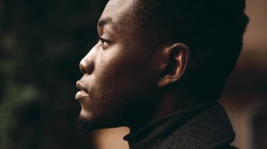 Odaklanmış bakışları olan, koyu renk elbiseli, içe dönük genç bir adam. Açık hava ortamında derin düşünce ve duyguları vurgulayan yakın plan portresi