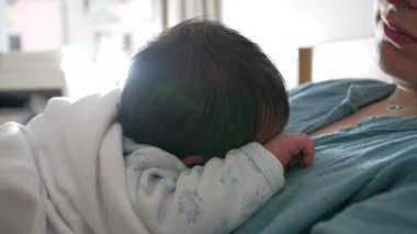 Yeni doğan bebek güneş ışığıyla annesinin göğsünde dinleniyor. Bebeğin kafasının etrafında halo etkisi yaratıyor. Samimi ve huzurlu bir an.