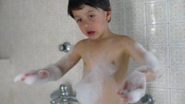 Köpük banyosundan zevk alan genç bir çocuk, köpükle kaplı, neşeli ifadeler takınıyor, eğleniyor, çocukluk anılarının neşe ve heyecanını neşeli sahnelerde vurguluyor.