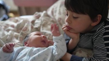 Ağabeyim yeni doğan bebeğe şefkatle bakıyor. Nazikçe dokunuyor, birbirine bağlanıyor. Yatak odası ayarları, sevgi ve merak ifadeleri, aile bağı, yeni kardeş ilişkisi.