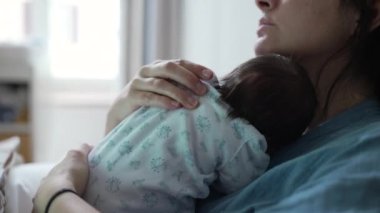 Anne, yeni doğmuş bebeğini yatakta otururken kucaklıyor, değerli ve samimi anı kucaklıyor, sıcak ve sevgi dolu bir ev ortamında derin bir bağ ve sevgiyi vurguluyor.