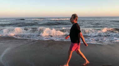 Retired Older senior man walking at the beach shore during sunset. Contemplative meditative thoughtful