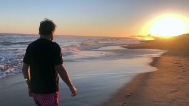 Older man walking at the beach during sunset, meditative senior person walks by the shore