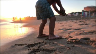 Baby toddler playing with sand at the beach, sunflare shining