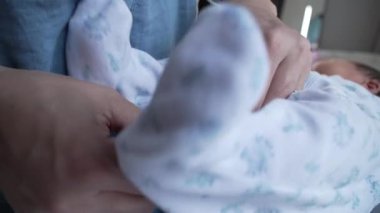 Ebeveyn, yeni doğmuş bir bebeğin kıyafetine küçük bir düğme iliştirir ve bebeğe gösterilen hassas ilgi ve ilgiyi ön plana çıkarır. Ayrıntılı hassas an