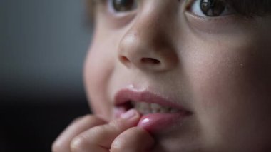 Yakından çekilen çocuk çenesiyle koltukta dinleniyor, ilginç bir şeyi gözlemlerken neşesini ifade ediyor.