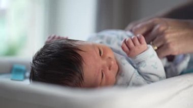 Yeni doğan bebeğin üstünü değişen bir masanın üzerinde yakın plan fotoğrafı, bebeğin bacağını tutan anne, bir evde rutin bebek bezi değiştirme sırasında etkileşimi yakalayıp bağ kuruyor.