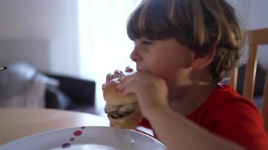 Evde hamburger yiyen sevimli küçük çocuk.