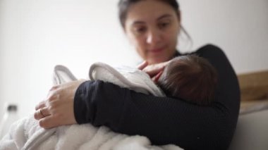 Anne sevgiyle bakarken yeni doğmuş bebeği emziriyor. Bebek yumuşak bir battaniyeye sarılmış, anne ve çocuk arasındaki bağ ve erken anneliğin samimi ve besleyici anı.