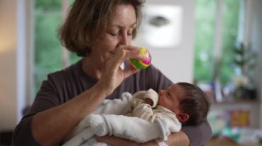 Büyükannenin yeni doğan torunuyla ilgilenmesi renkli bir oyuncakla, rahat bir ev ortamında, bağ, bakım ve iki nesil arasındaki gelişim etkileşimiyle