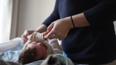 Anne yeni doğmuş bebeği giydiriyor, nazikçe kol kola giriyor, özen ve ilgiyi vurguluyor, bağ kurmanın hassas anlarını yakalıyor, sevgi gösteriyor, bebek bakımının ilk aşamalarını gösteriyor.