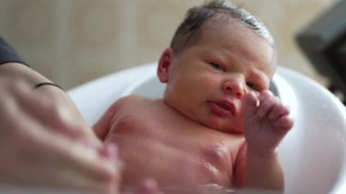 Banyo sırasında yeni doğan bebek, düşünceli bir ifadeyle etrafına bakıyor, merak ve farkındalık anı, anne tarafından sağlanan bakımı yansıtıyor.