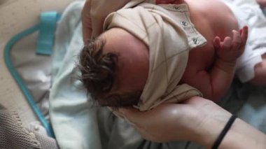 Anne yeni doğmuş bebeği giydiriyor, tişörtünü kafasının üstüne kaldırıyor, hassas bir ilgi anı, ebeveyn sevgisinin ve ilgisinin vurgulanması, bebek bakımının erken aşamaları, samimi ve besleyici sahneler.