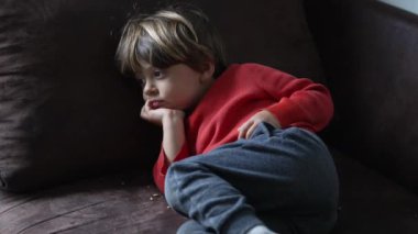 Rahat kış giysileri içinde, üzerinde düşünceli bir görünüm ve her yerde pişmiş mısır bulunan koltuklara yaslanan çocuk.