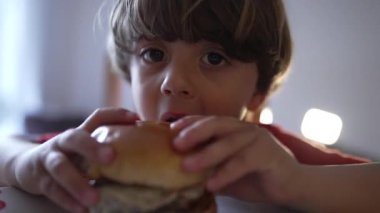 Gün boyunca yemek masasında nefis bir el yapımı burgerin tadını çıkaran genç çocuğun yakın çekim yüzü.