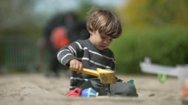 Oyun sahasında kum kuyusu kazma oyunu - Çocuk, Güneş Altında Yerdeki Delikleri Kazmak İçin Küçük Plastik Kürek Kullanıyor