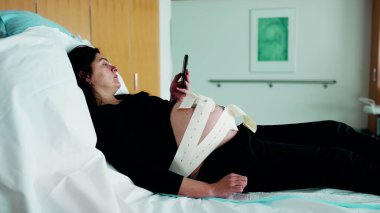 Ultrason kayışlı annenin bebeğin kalp atış frekansını kontrol etmesini ve Prelabor Kasılmalarını Beklerken Telefonu Kontrol etmesini bekliyorum.