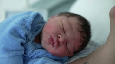 Yeni doğan bebeğin yüzünün, hayatının ilk gününde annesinin göğsünde dinlenirken yakın plan görüntüsü. Doğumdan sonra hastanedeki ilk günlerinde şirin bir bebek.