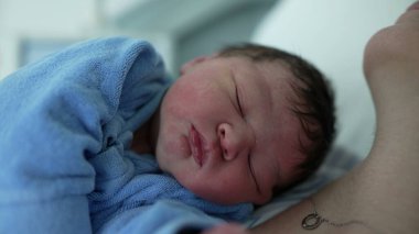 Yeni doğan bebeğin yüzünün, hayatının ilk gününde annesinin göğsünde dinlenirken yakın plan görüntüsü. Doğumdan sonra hastanedeki ilk günlerinde şirin bir bebek.