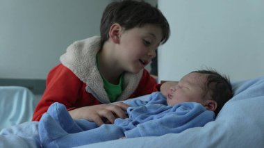 Ağabeyi, yeni doğan kardeşiyle sevgi dolu bir şekilde etkileşim içinde. Sevgi dolu sevgi dolu anlar ve kardeş bağı kuruyor. Aile sevgisi, ilgi ve bağlılık temaları için mükemmel.