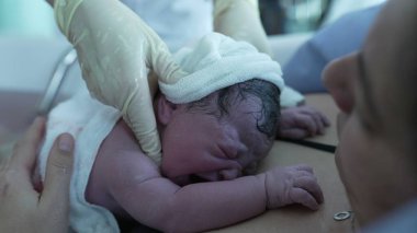 Yeni doğan bebeğe doğumdan sonra yakın çekim, hayatın ilk saniyeleri, hemşirenin eli sıcacık giysiler, hayatın ilk dakikaları.