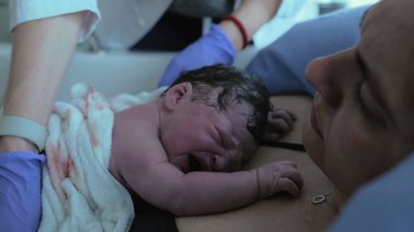 Doğumdan hemen sonra yeni doğmuş bir bebeğin ilk saniyeleri annesinin göğsünde dinlenmek için çırpınıyor deriyle teması vurguluyor, bir insanın ilk ağlayışları...
