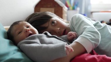 Büyük kardeş yeni doğmuş bir bebeğe sarılıp sıcak bir ev ortamında sevgi dolu bir anı paylaşıyor.