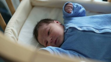 Yeni doğmuş bebek beşikte, mavi giyinmiş, merakla etrafa bakıyor. Erken yaşam, masumiyet ve çocuk odasının rahat ortamı. Ebeveynlik ve yeni doğan bakımı konuları için ideal