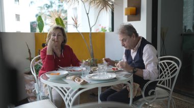 Bitkilerle süslenmiş Serene Patio 'da Kahvaltı Yapan Yaşlı Çift