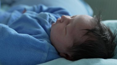 Yeni doğmuş bebek mavi bir battaniyenin üzerinde, rahat mavi bir elbise içinde yatıyor. Bebek mışıl mışıl uyuyor. Yumuşak kumaşın altına sıkıştırılmış minik elleri var. Huzur dolu ve saf bir masumiyeti temsil ediyor.