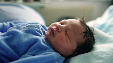 Yeni doğan bebek mavi tulumuyla mışıl mışıl uyuyor. Yüzünde barışçıl bir ifade var. Bebekliğin sakin ve hassas anları tasvir edilir, saf masumiyeti yakalar.