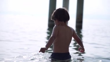 Oğlan, arka plandaki dağlarla sıcak yaz gününde Kristal berrak gölde yıkanırken manzaraya hayran.