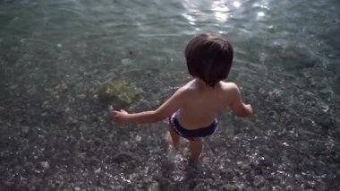 Top View - Güneşli yaz gününde serinlemek için Crystal Clear Gölü 'ne giren ve küçük çakıl taşlarıyla kaplı bir çocuk