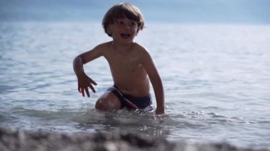 Gülümseyen Çocuk, arka plandaki dağlarla serinletici yaz oyununda Crystal Clear Gölü 'nden koşarak ortaya çıkar.