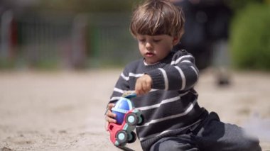 Genç Çocuk, gün boyunca çizgili kazakla oyun parkındaki çimento kamyonuna kum dolduruyor.