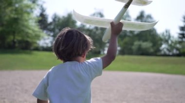 Enerjik Çocuk Oyuncak Uçakla Koşuyor, Güneşli bir günde açık hava parkı eğlencesinde onu fırlatmaya hazır.
