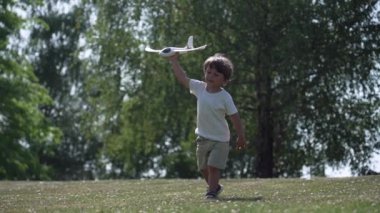 Küçük Çocuk Oyuncak Planör Lisesi 'ni elinde tutuyor, sonra Wooded Park' taki oyun sırasında fırlatma momentumu kazanmak için kameraya doğru koşuyor.