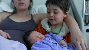 Kardeşi, yeni doğan bebeğe sevgiyle bakar. Annesinin yanında oturur. Kardeşler ve ömür boyu sürecek bir ilişkinin başlangıcı arasındaki hassas bağı vurgular.