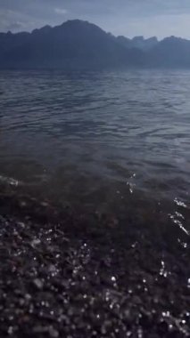 Tatlı su sahili, hareket eden gölle kumsala yakın çekim, arka planda dağlar.