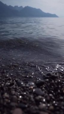 Tatlı su sahili, hareket eden gölle kumsala yakın çekim, arka planda dağlar - suya yansıyan güneş