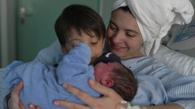 Anne ve çocuğu, doğumdan sonra kucağında bebeğiyle hastaneye geliyor. Hemşire küçük bebeği klinikte annesinin yanında kardeşinin koluna veriyor. Kardeşler ilk kez kaynaşıyor.