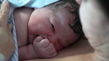 Doğumdan hemen sonra yeni doğan bebek yüzü. Doğumdan dakikalar sonra dünyaya geliyor. Annenin teniyle temasta bulunuyor.